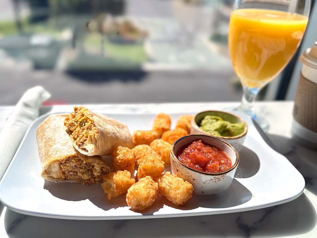 Beachside breakfast burrito, tater tots, salsa, and guacamole at Sundrift Inn on a white plate.