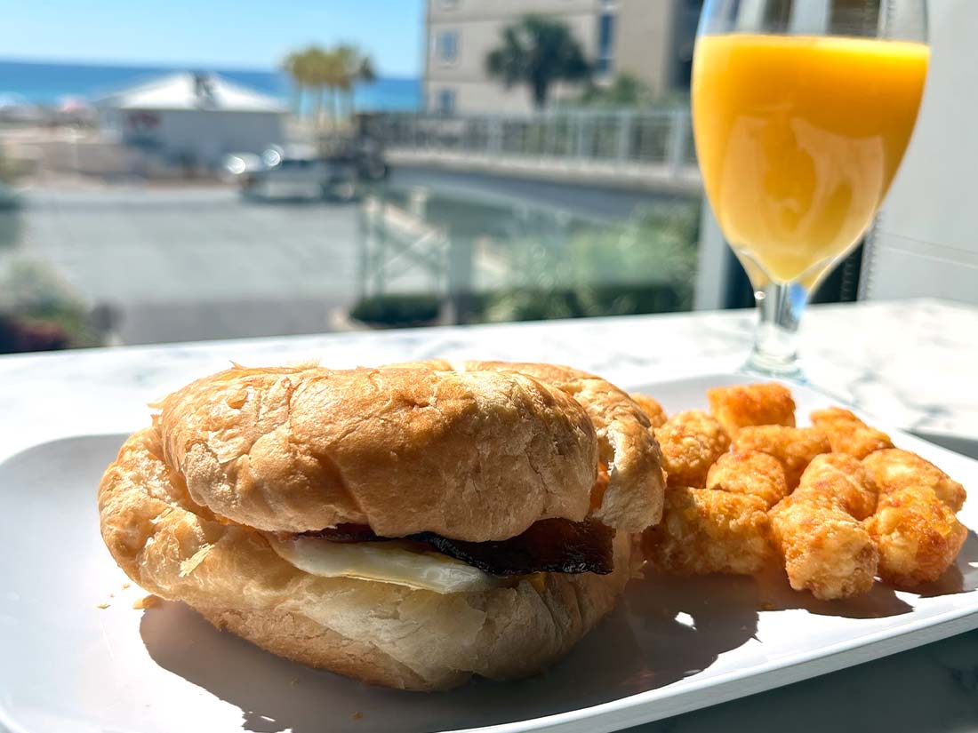Breakfast sandwich, tater tots, and orange juice at a beachside Panama City Beach Hotel window view.