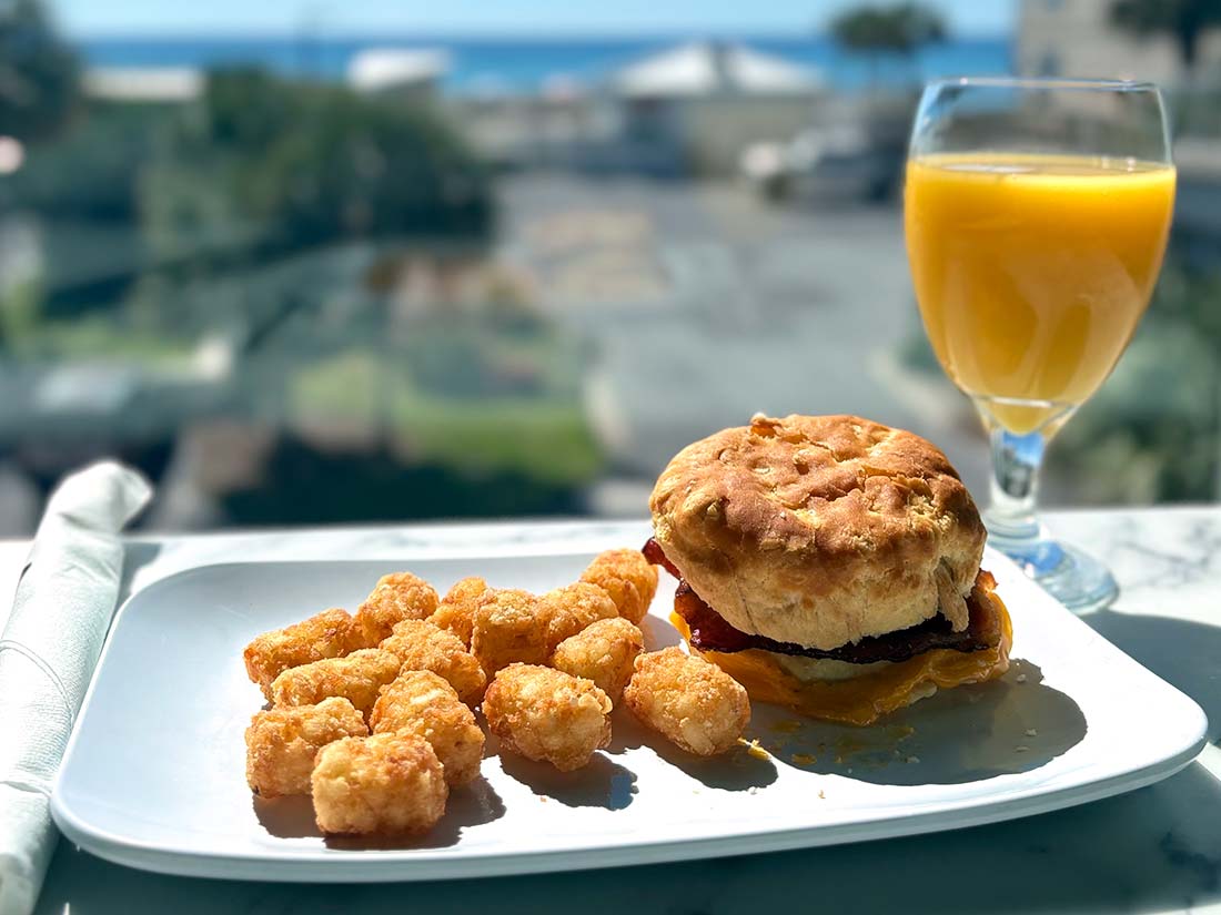 Breakfast sandwich, tater tots, and OJ by a sunny window at Sundrift Inn Panama City Beach Hotel.