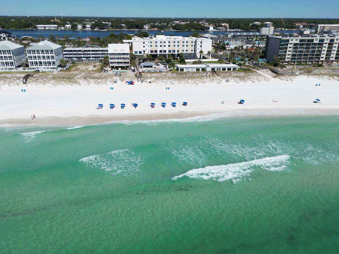 Aerial view of beachside hotels with blue umbrellas near Panama City Beach Hotel rooms.