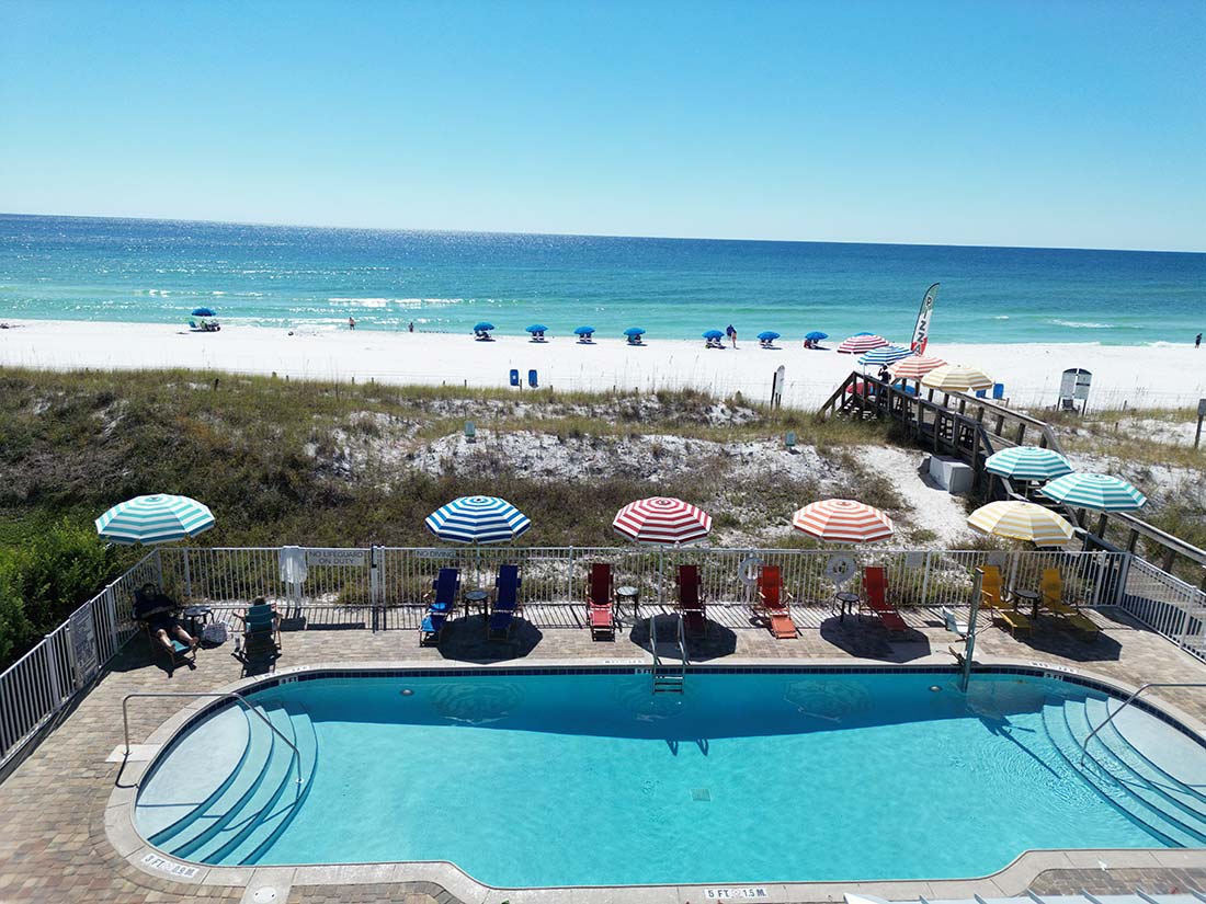 Beachside swimming pool with colorful umbrellas, lounge chairs, and ocean views at Sundrift Inn.