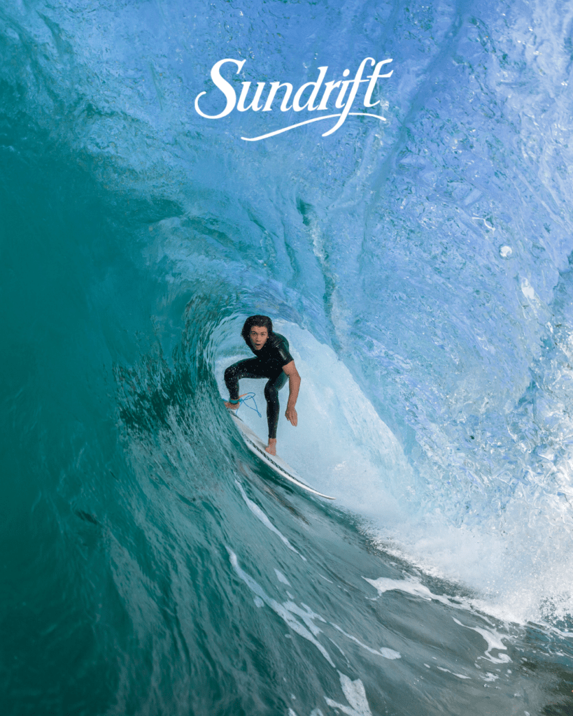 Surfer riding a wave near Okaloosa Island on Florida’s Emerald Coast with Sundrift beachfront views