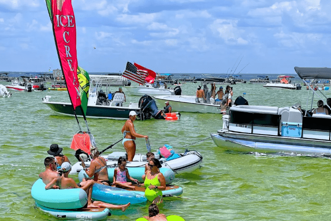 Visitors floating and relaxing in shallow water at Crab Island Destin Florida with boats anchored nearby