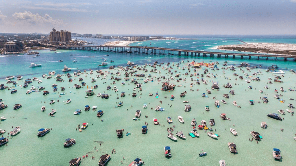 Aerial view of Crab Island sandbar near Destin Bridge with boats gathered in clear emerald water on Florida’s Emerald Coast