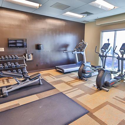 Small gym room with free weights, treadmill, two ellipticals, and two exercise mats.