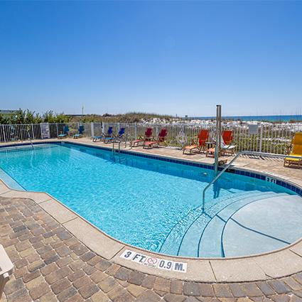 Outdoor swimming pool with lounge chairs, clear blue sky, and ocean visible in the background.