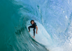 Surfer riding a wave near Okaloosa Island on Florida’s Emerald Coast with Sundrift beachfront views